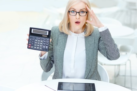How can it be. Surprised nice professional business woman holding calculator and feeling shocked while being involved in workの写真素材