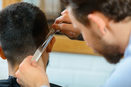 The best hair cut. Close up of scissors in hands of professional barber holding them and concentrating on work while making hair cutの写真素材