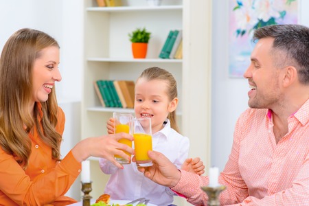 Cheers. Nice delighted happy family sitting at the table and drinking juice while having festive dinnerの写真素材