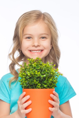 Girl with flower. Little girl is smiling brightly while holding green plant in flowerpot.の写真素材