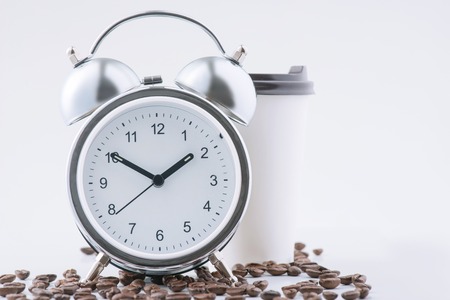Average morning. Alarm clock, coffee beans and papercup filled with fresh drink are waiting for its...