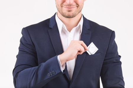 Safety measures. Smiling man putting condom into his breast pocket.