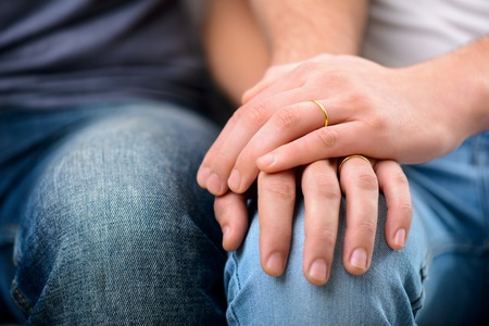 Close up of hands of two homosexuals holding them together and resting while sitting on the sofa