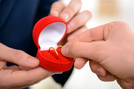 Close up of ring in  hands of pleasant guy taking it while celebrating wedding with his male partner