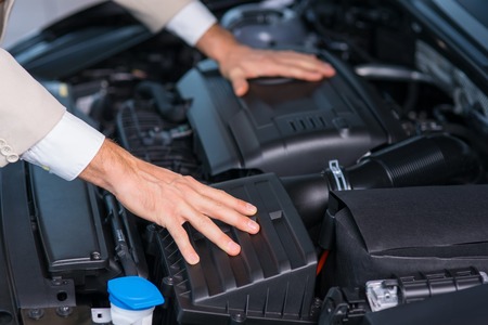 Close up of opened bonnet of the car with professional sale assistant checking the auto
