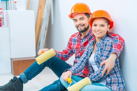 Cheerful smiling loving couple holding rolls and sitting on the floor while relaxing after pointing...