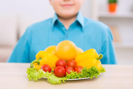 Good choice. Smiling chubby boy is standing in front of fresh vegetables on a plate.の写真素材