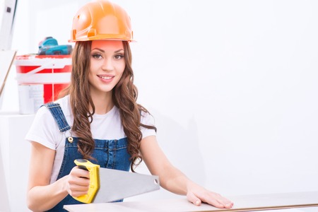 Sawing procedure. Young attractive girl in male role is sawing a chipboard.の写真素材