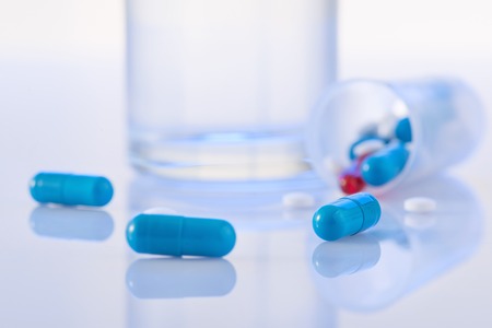 Remedy to take. Few pills are lying on the surface along with glass of water on the background.