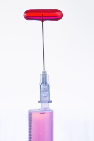 Needle in pill. Syringe in vertical position with a pill on top of its needle. の写真素材