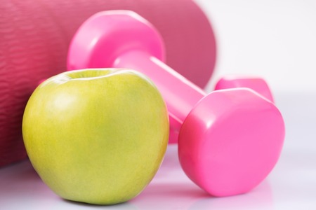 Weight-losing activity. Dumbbells along with an apple and yoga mat are on the surface.の写真素材