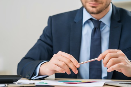 Concentrated on work. Serious diligent office worker sitting at the table and holding pen while being involved in workの写真素材