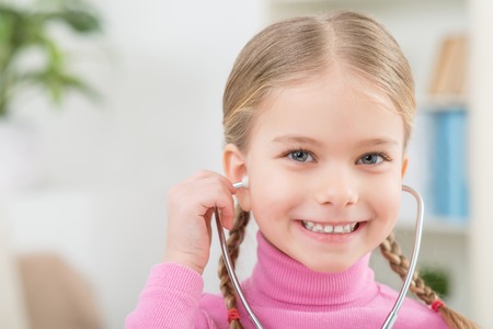 Want to be a doctor. Cheerful cute little girl holding stethoscope and playing with it while feeling happyの写真素材