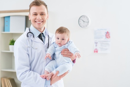 Like my job. Overjoyed smiling professional pediatrician holding infant and smiling while feeling happy to work with childrenの写真素材