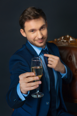 Toast for you. Close up of chalice of champagne in hands of confident cheerful businessman holding it while going to drinkの写真素材