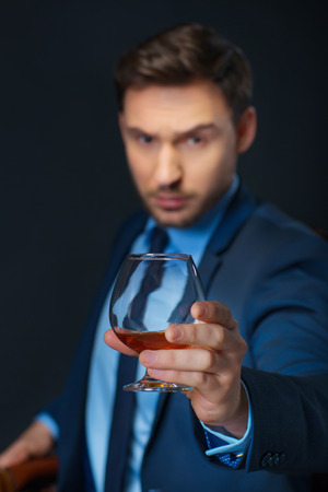 Way to success. Close up of glass of cognac in hands of handsome confident man holding it and going to drink while standing isolated on black backgroundの写真素材