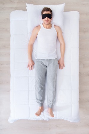Time to rest. Top view of pleasant man in sleeping mask lying on his back in bed while sleepingの写真素材