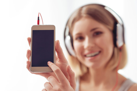 Device specialties. Attractive young woman is holding up a mobile phone while standing against whiteの写真素材