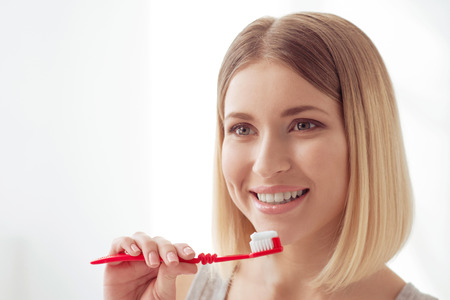 Morning procedures. Young attractive woman is holding toothbrush and smiling while taking care of...