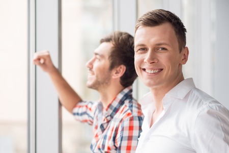Enjoy the view. Cheerful delighted man standing near window and together and expressing joyの写真素材