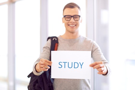 Involved in study process. Shit of paper in hands of smart positive student holding it while standing near windowの写真素材