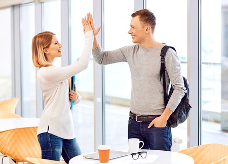 High five. Pleasant student standing near window and welcoming each other while giving five