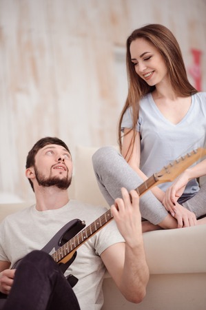 Love you deeply. Pleasant handsome guy playing the guitar and looking at his girlfriend while expressing his feelingの写真素材