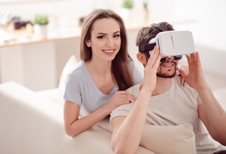 Try it. Pleasant young loving couple expressing gladness and trying virtual reality device while...