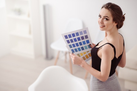 What to choose. Cheerful content beautiful woman holding cards with colors and smiling while being busy at workの写真素材