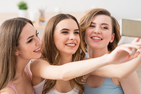 Memorize this moment.  Cheerful delighted smiling girls holding smart phone and making photos while having funの写真素材