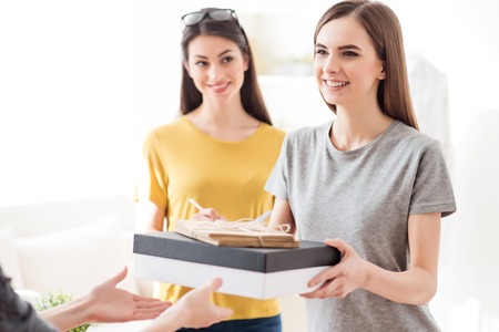 Best service for you. Pleasant positive smiling girl holding box and giving it to her client while standing with the colleagueの写真素材