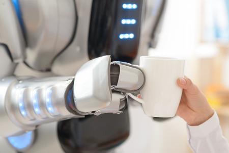 Close up of cup of coffee in hands of robot holding it and giving to a nice girlの写真素材