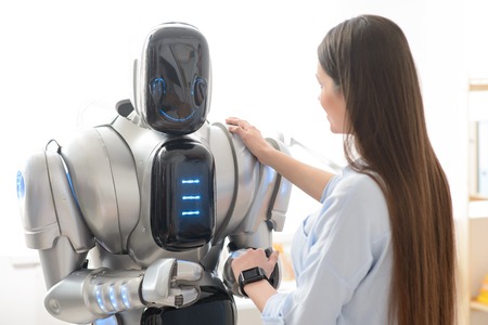 Pleasant delighted girl holding her hand on the shoulder on the robot while shaking handsの写真素材
