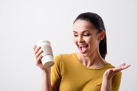 Positive smiling content joyful woman drinking coffee and expressing gladness while standing isolated on grey backgroundの写真素材