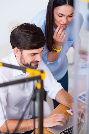 Selective focus of delighted positive colleagues working on the laptop while 3d printer working on...