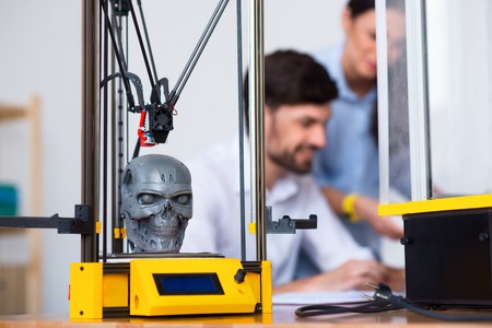 Selective focus of 3d printer working on the table while positive colleagues using  the laptop in the backgroundの写真素材