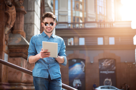 Lighten up my mood.  Positive content handsome man smiling and using tablet while leaning on the handrailの写真素材