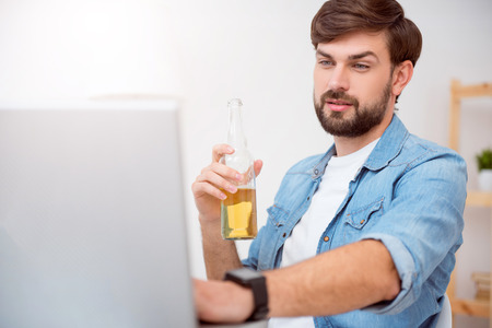 I almost finishing. Handsome bearded man using his laptop and looking at the screen while drinking a beverageの写真素材