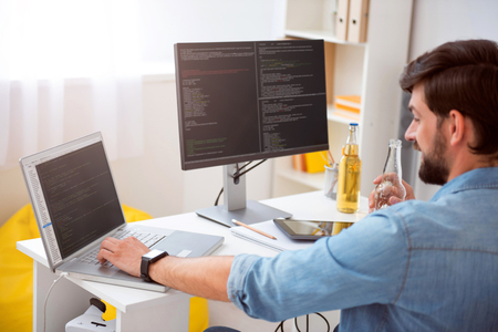 Today is a good day. Delighted young man having a drink while programming on his computer