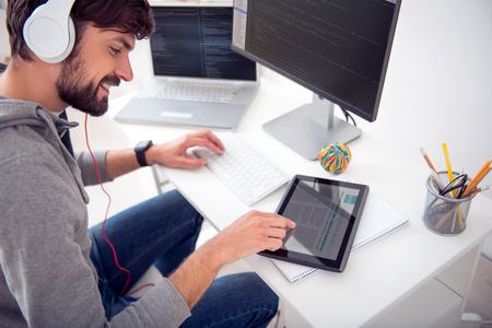 Something interesting. Top view of a cheerful handsome man using his tablet while writing codes on...