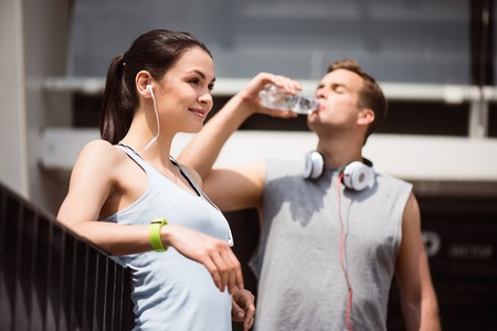 It is a good day. Pretty tired young woman listening to music after working out while a man drinking water in the backgroundの写真素材