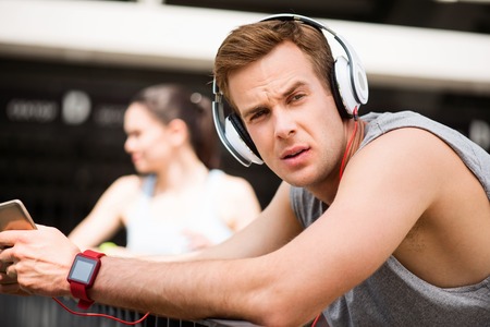 Training as a part of my day. Serious pensive sport man using a headset with a woman standing in the backgroundの写真素材