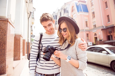 Being in good spirits. Cheerful and positive young lovely couple travelling together being in a big city, holding a camera and watching new photosの写真素材