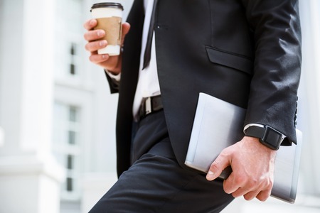 My ordinary day. Close up of tablet in handsome pleasant businessman holding it and drinking coffee while going to workの写真素材