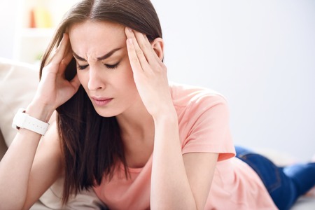 Terrible tortures. Sick young woman holding her temples and closing her eyes while having a headacheの写真素材