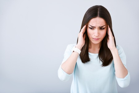 Can not overcome pain. Pleasant beautiful sick woman touching her temples and having a headache while standing isolated on white backgroundの写真素材