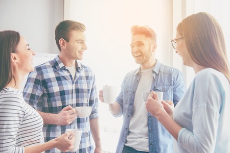 Best team. Positive and laughing young business people talking while coffee break in their office and enjoying their timeの写真素材