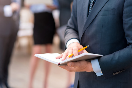My everyday helper. Close up of notebook in hands of pleasant businessman holding it while his colleagues working in the backgroundの写真素材