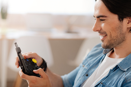 My childish hobby. Positive delighted smiling man holding game console and playing video games while...