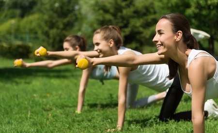Work with enthusiasm. Cheerful beautiful smiling women holding dumbbells and doing sport activities with them while expressing joyの写真素材